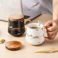 Nordic-inspired ceramic coffee mug, teacup, and saucer set with gold-traced marble pattern and wooden lid